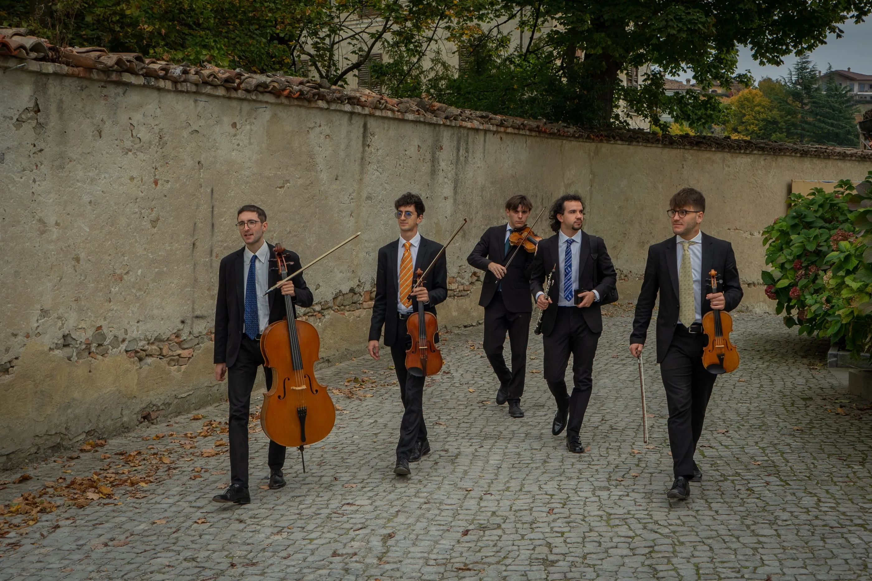 I musicisti dell'Ensemble Belliners camminano con i loro strumenti lungo un vicolo acciottolato